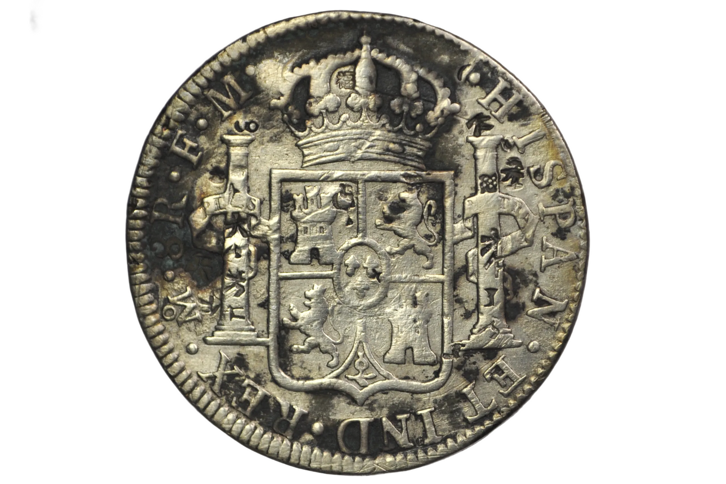 Reverse of a panish 8 reales from 1784. Two pillars on either side of a crest that is topped by a crown above. Lettering: Mo.8R.F.M. Hispan. ET IND.REX
