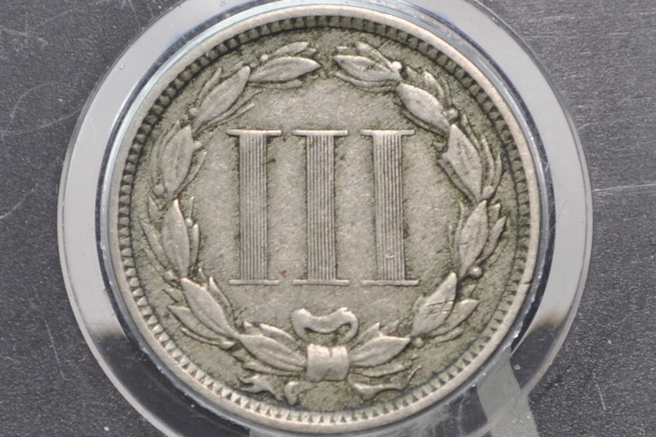 Silver coin with three vertical bars and wreath design on a dark background