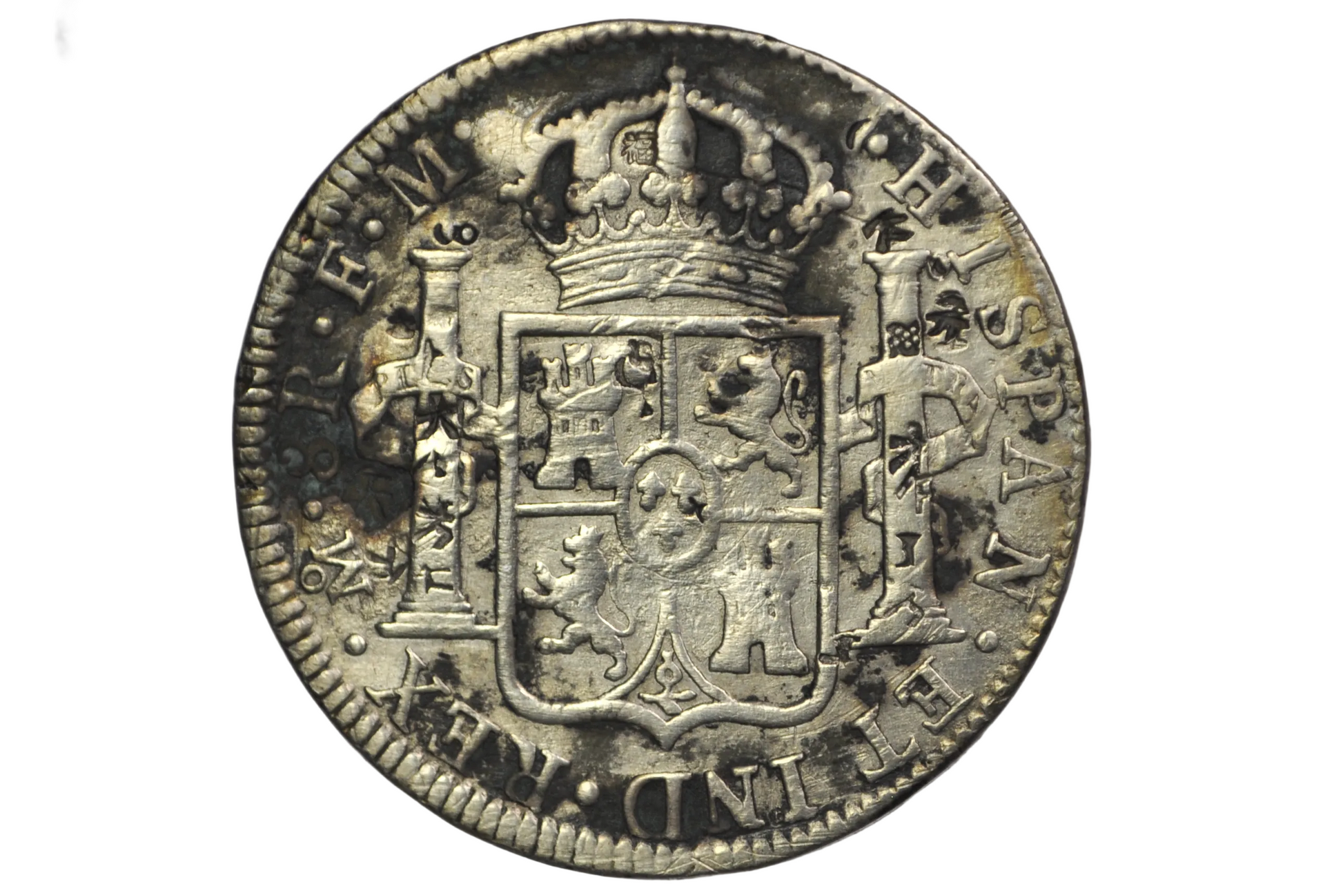 Reverse of a panish 8 reales from 1784. Two pillars on either side of a crest that is topped by a crown above. Lettering: Mo.8R.F.M. Hispan. ET IND.REX
