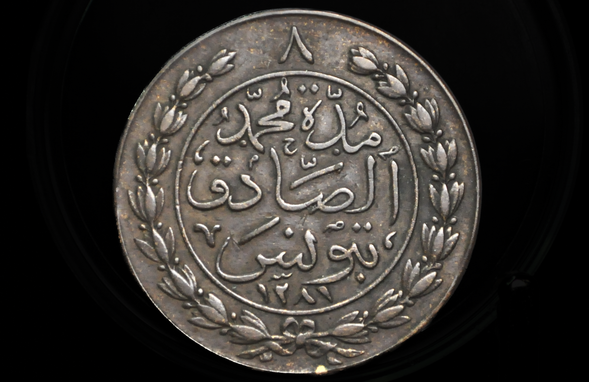 Large Copper coin with Arabic text and floral design on a black background. Tunisia Coin 8 Kharub from 1865