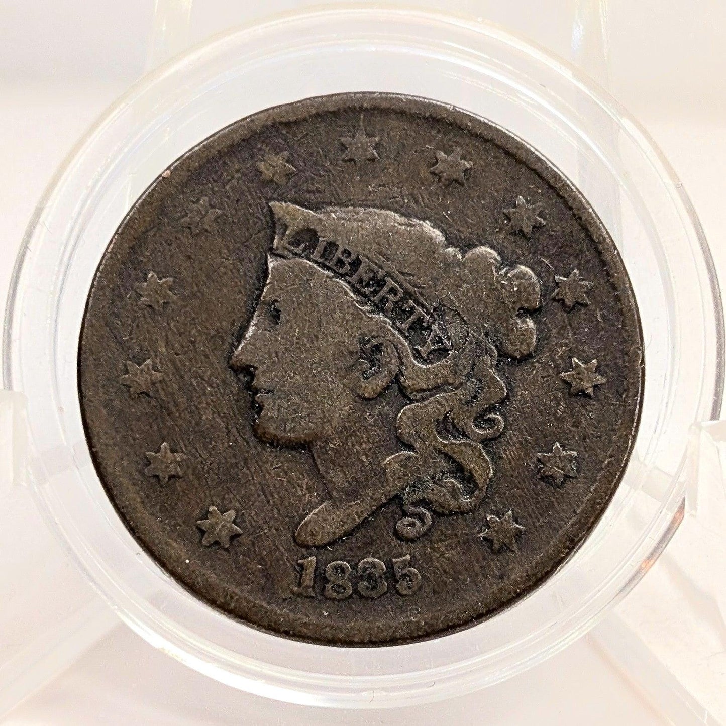 Vintage coin with a profile of a person and the year 1835, encased in clear plastic.