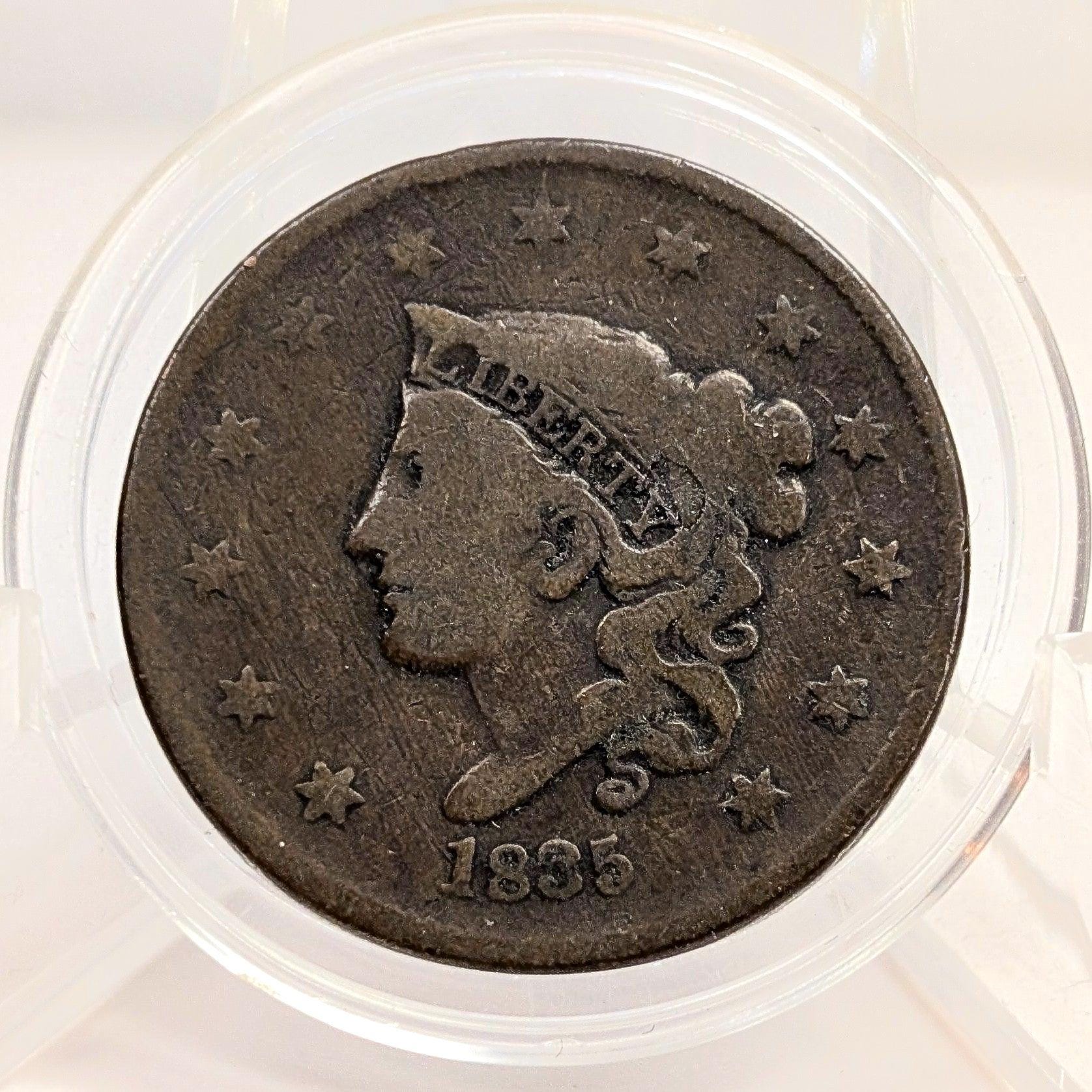Vintage coin with a profile of a person and the year 1835, encased in clear plastic.