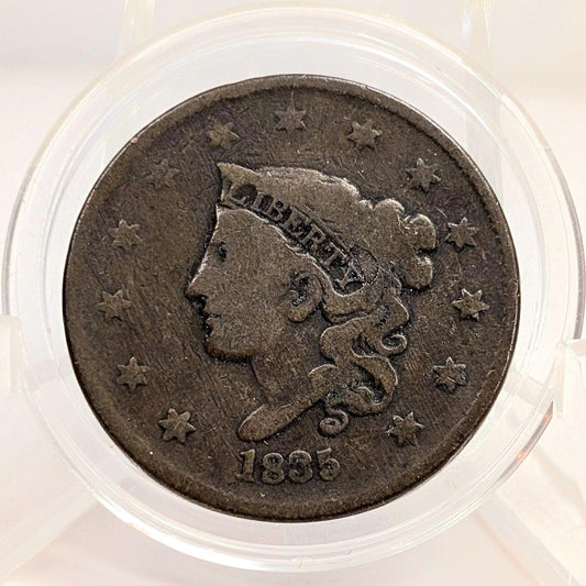 Vintage coin with a profile of a person and the year 1835, encased in clear plastic.