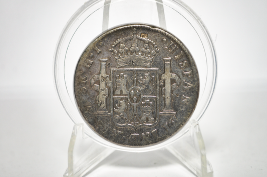A vintage silver coin featuring the coat of arms of Spain, displayed inside a clear circular protective capsule on a white background.