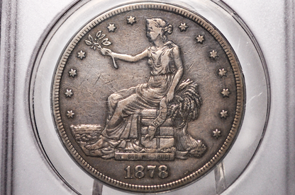 An 1878 United States silver trade dollar coin inside a clear plastic grading holder, showing the seated Liberty design with the year 1878 at the bottom.
