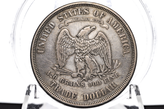 A silver-colored United States Trade Dollar coin sealed inside a clear plastic protective capsule, displayed on a clear stand against a white background.