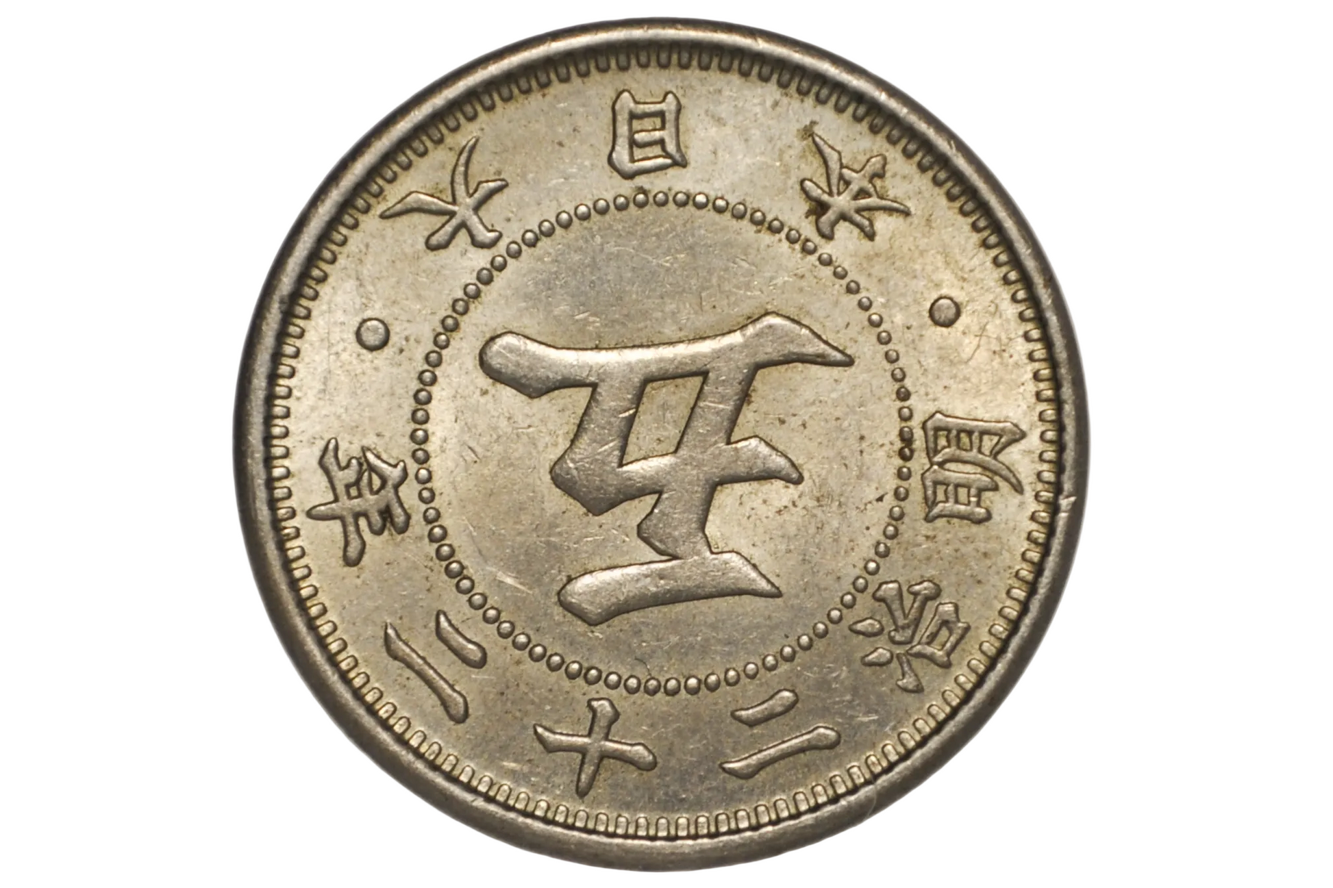 A close-up of a Japanese silver coin inside a clear plastic protective capsule, showing the central kanji character for five and surrounding Japanese text.