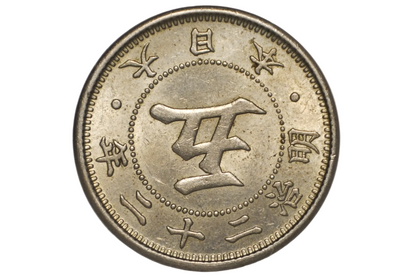 A close-up of a Japanese silver coin inside a clear plastic protective capsule, showing the central kanji character for five and surrounding Japanese text.
