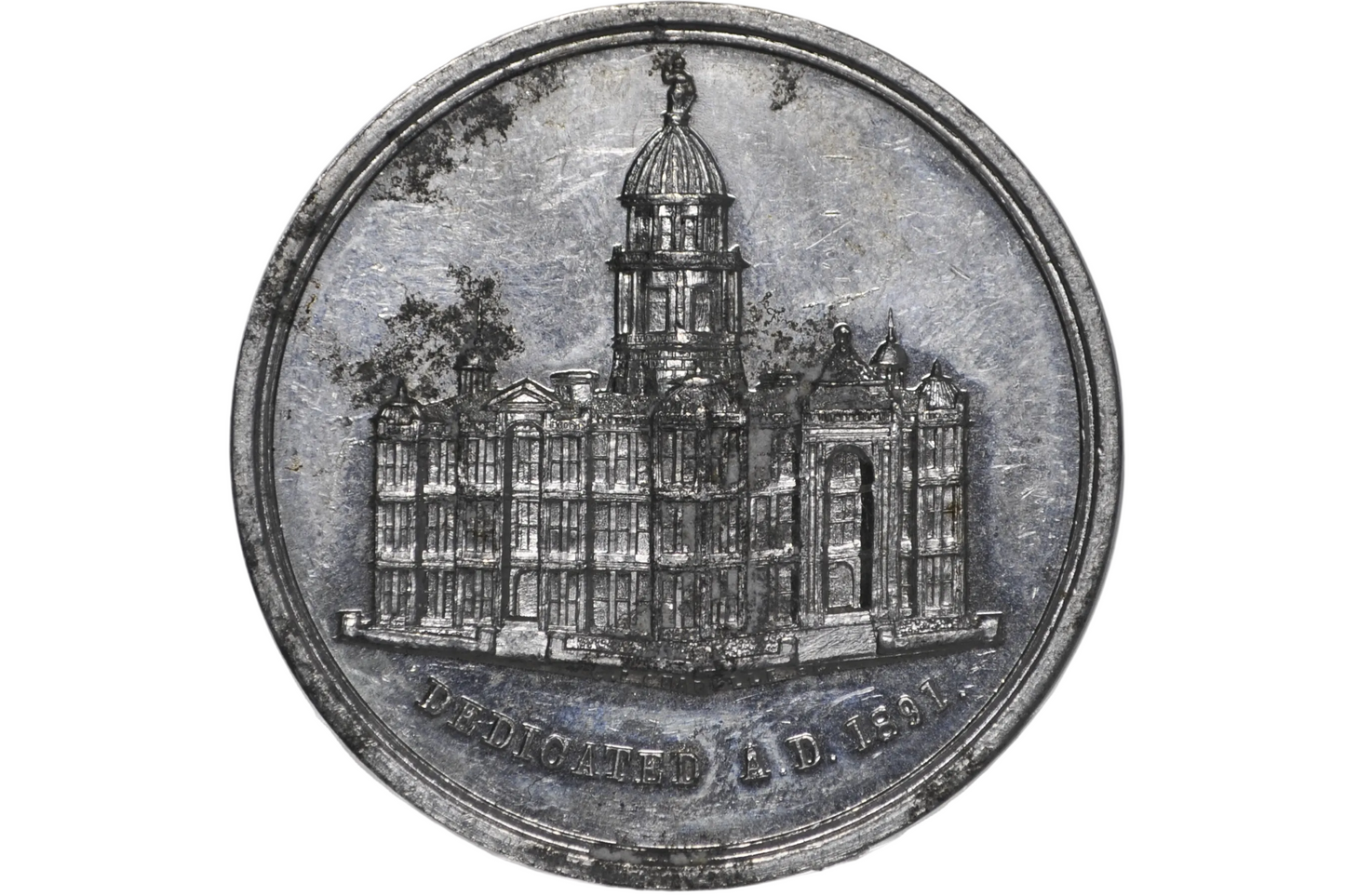 A round silver-toned commemorative coin or medallion featuring an engraved building with a dome from 1891 california