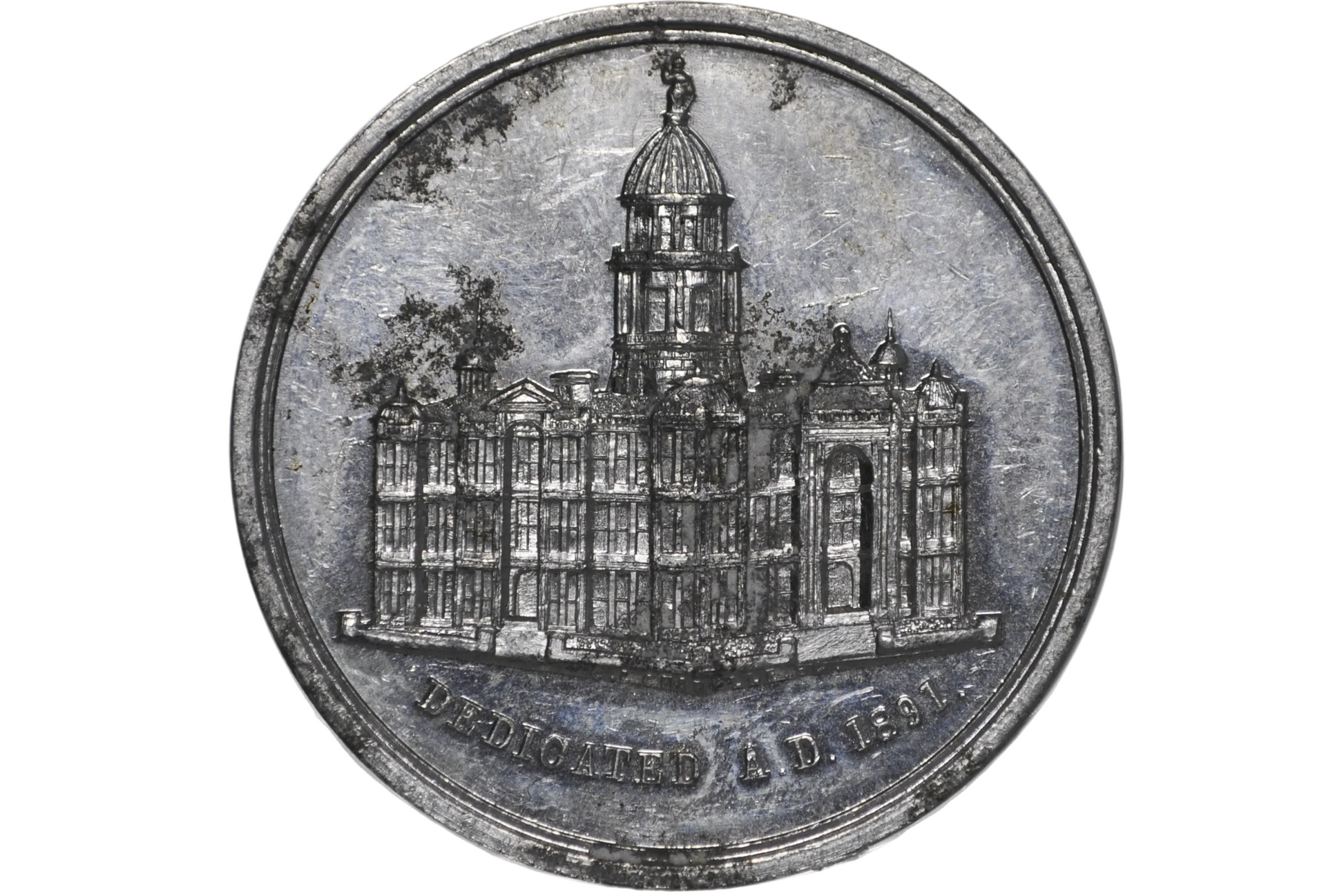 A round silver-toned commemorative coin or medallion featuring an engraved building with a dome from 1891 california