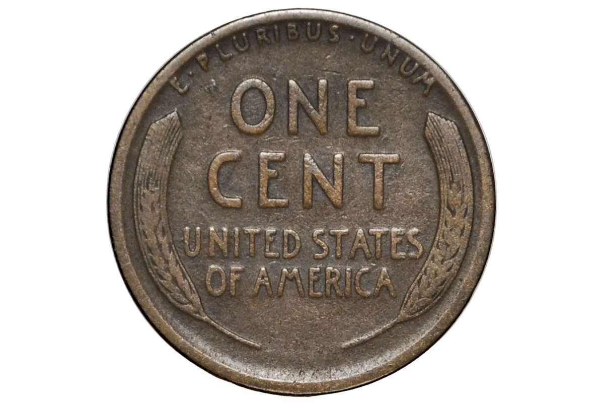 A close-up of a vintage United States one-cent coin inside a clear protective capsule, showing the reverse side with 'ONE CENT', 'UNITED STATES OF AMERICA', and wheat motifs.
